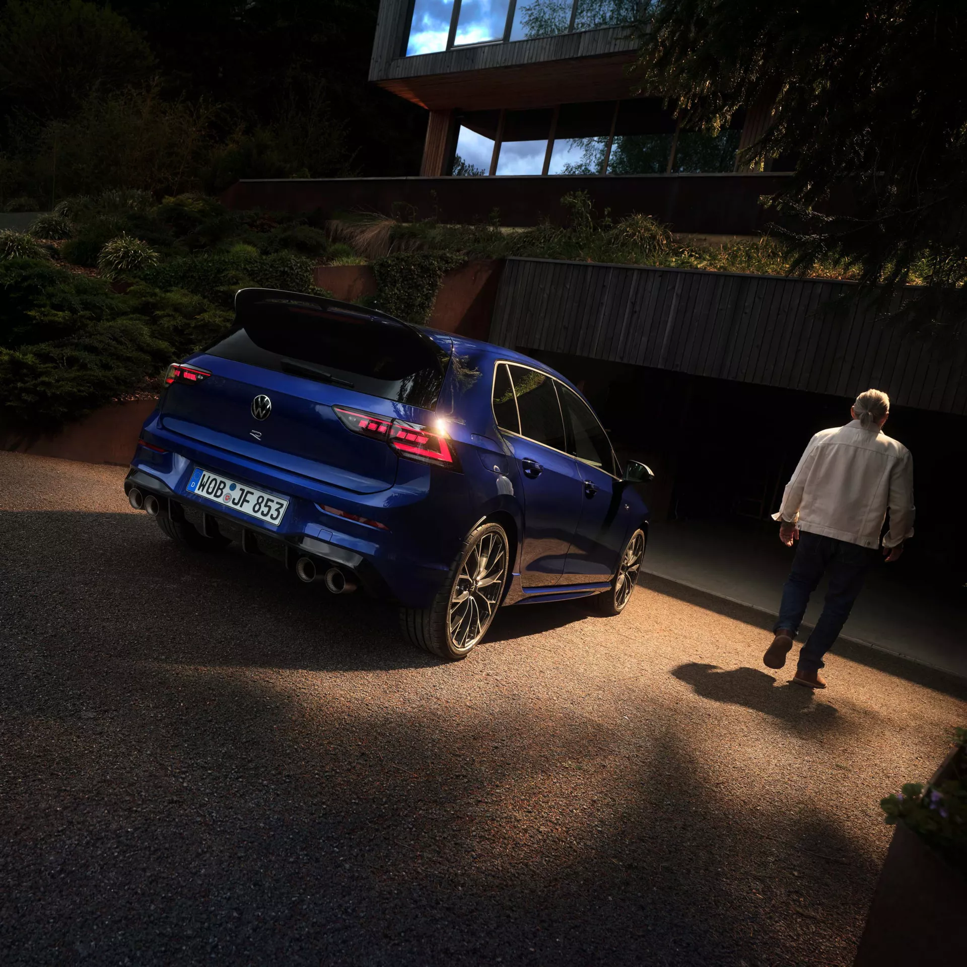 zu sehen ist ein blauer Golf von hinten vor einem Haus. Daneben geht eine Person