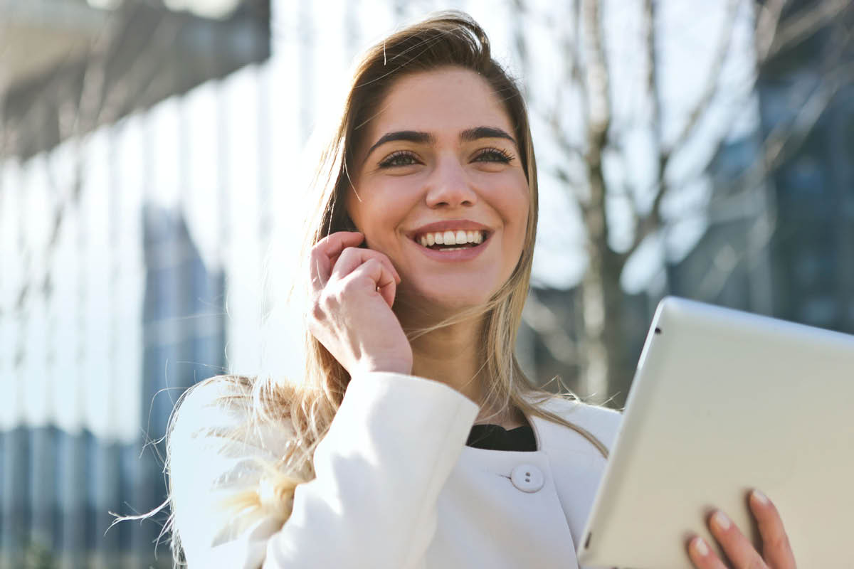 zu sehen ist eine glückliche Frau mit Handy und Tablet