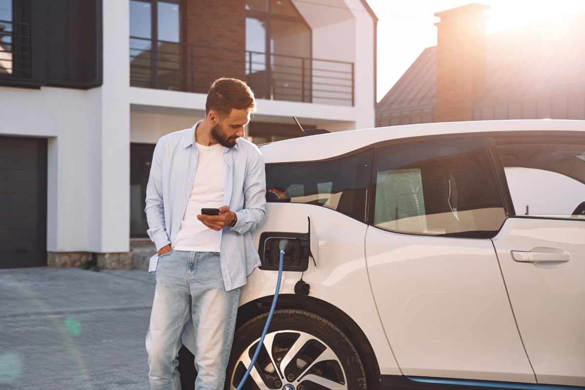 zu sehen ist ein E-Auto an der Ladesäule. Daneben steht ein Mann und wartet